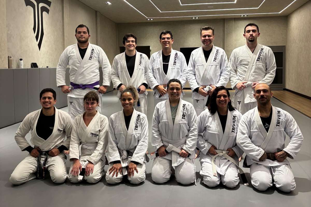 Turma adulta mista da Trivium Jiu-Jitsu, homens e mulheres de kimono reunidos no tatame ao final do treino