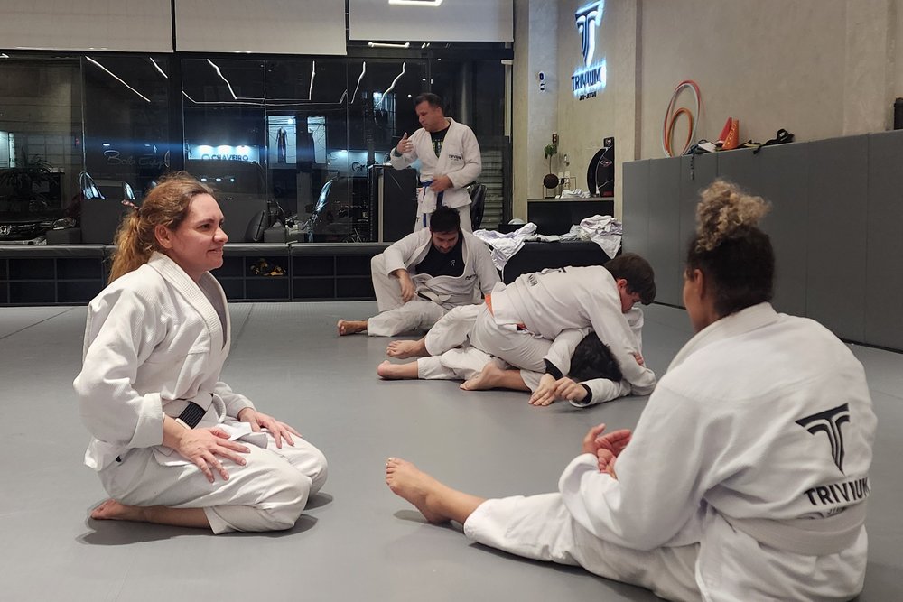 Alunas sentadas no tatame da Trivium observando o professor durante a explicação da técnica