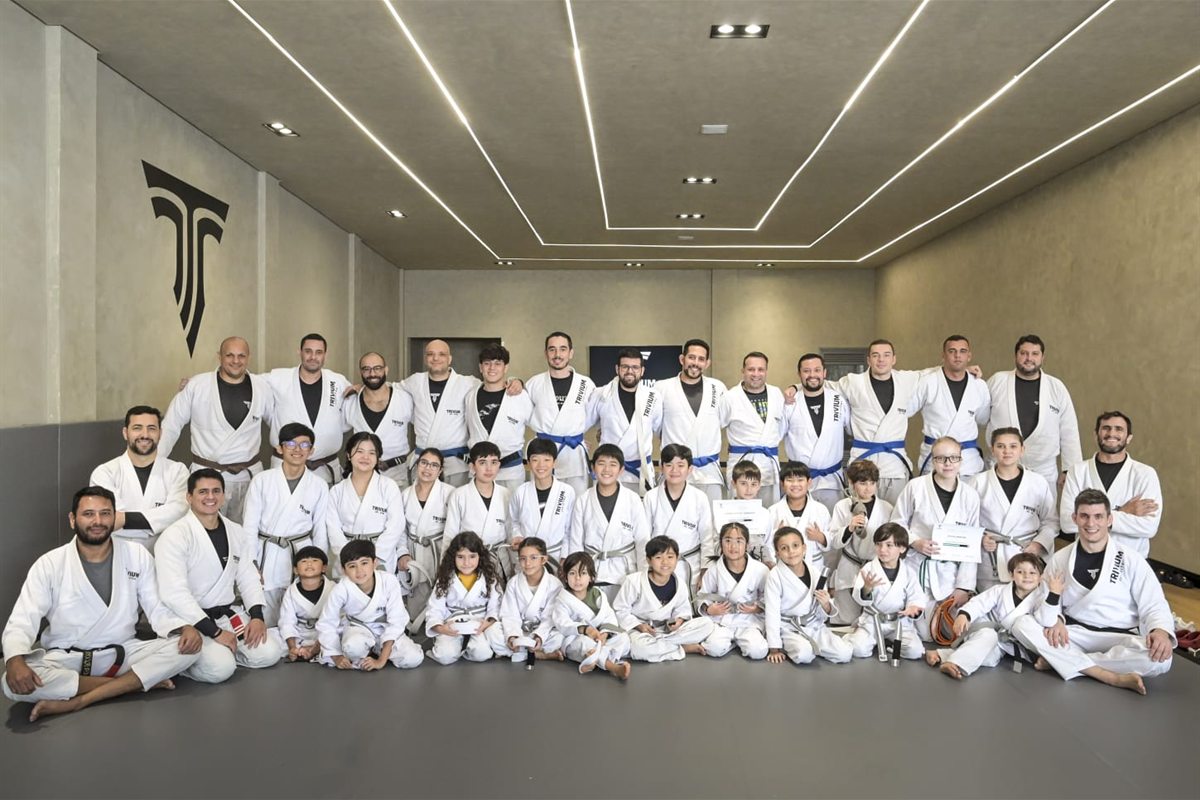 Alunos adultos e crianças da Trivium Jiu-Jitsu reunidos de kimono no tatame