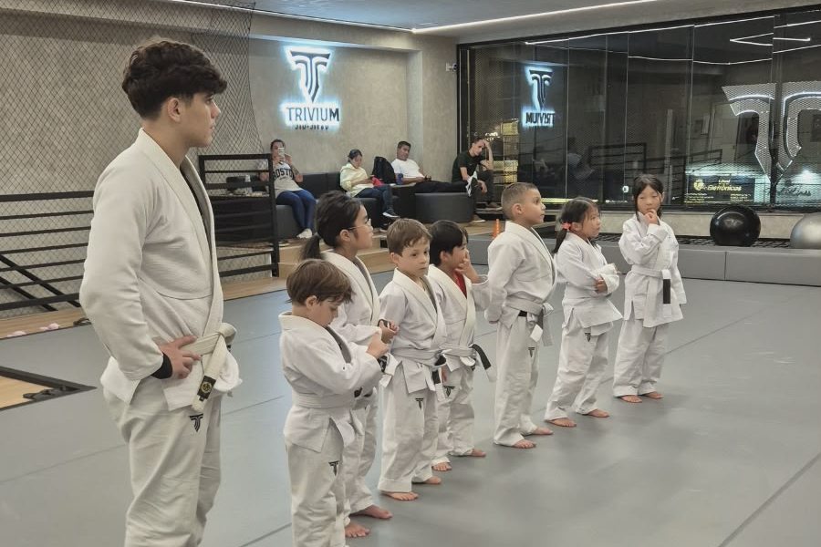 Turma infantil de kimono perfilada no tatame ao lado do professor da Trivium
