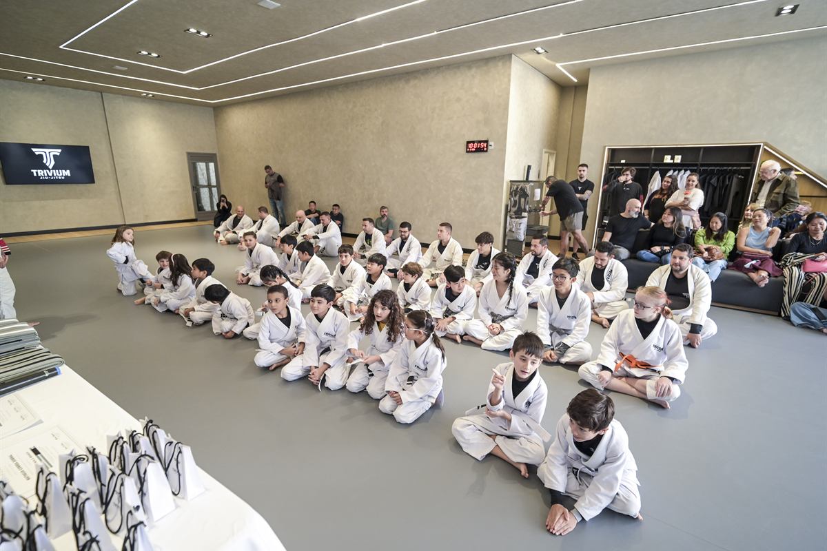 Turma infantil de kimono sentada no tatame da Trivium Jiu-Jitsu durante a cerimônia de graduação