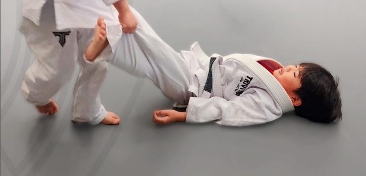 Criança pequena de kimono deitada no tatame durante um exercício da aula infantil